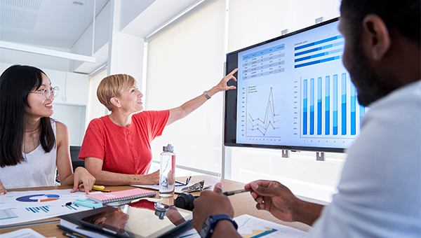 Business people reviewing analytics data on a wall-mounted monitor