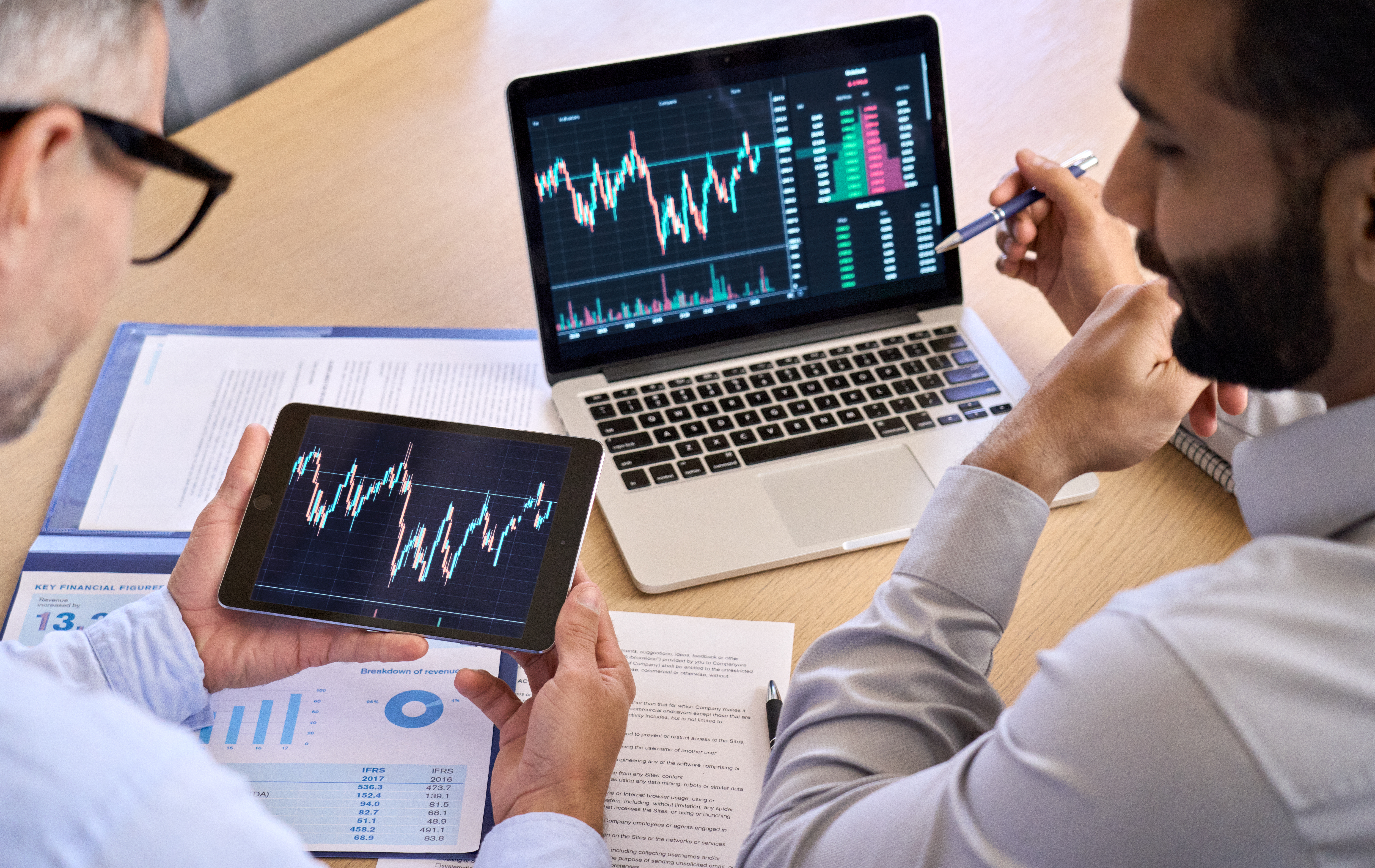 Businessmen checking data graphs on a laptop and a tablet