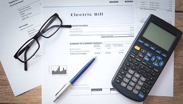 An electric bill with glasses, a scientific calculator and a pen