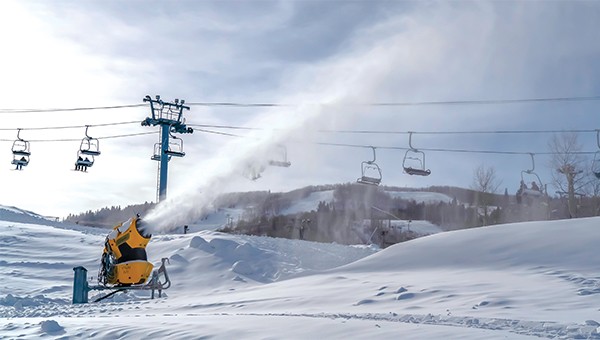 snow blower machine on a ski slope with ski lifts in the background