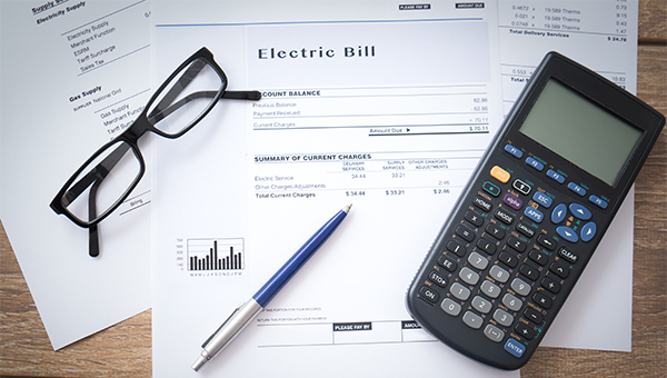 An electric bill with glasses, a scientific calculator and a pen An electric bill with glasses, a scientific calculator and a pen