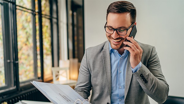 Man smiling with talking on his mobile phone flipping through a folder